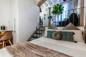 A bedroom with a bed, a chair, a desk, a staircase, and a large plant.