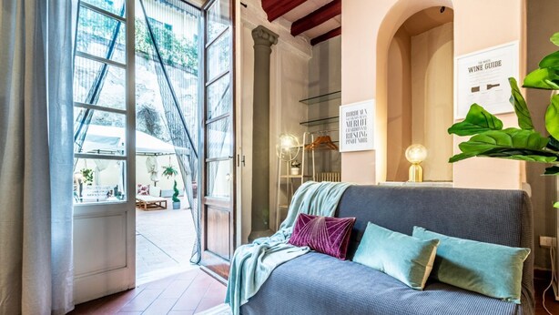 A cozy room with a grey sofa, a patterned rug, and a large window with a view of the outside. - Wine Apartments Florence Vernaccia (Firenze)