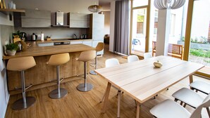 A modern kitchen with a central island, wooden flooring, and a dining area with a light-colored table and white chairs.