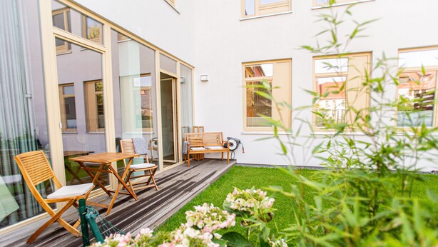 A modern house with a wooden deck, outdoor seating, and a well-maintained garden.