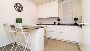 A modern kitchen with white cabinets, a black countertop, and two white folding chairs. - Deluxe Apartment Juan Bravo Suites I (Madrid)