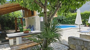 Une piscine en pierre avec une terrasse en bois, un banc en bois et un petit palmier.