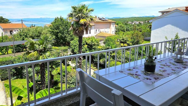 Un balcon avec une table et une chaise blanches, donnant sur un jardin luxuriant et offrant une vue sur la côte.