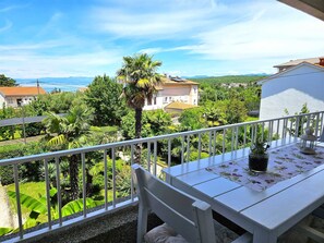 Un balcon avec une table et une chaise blanches, donnant sur un jardin luxuriant et offrant une vue sur la côte.