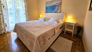 Une chambre à coucher avec un lit, deux tables de chevet, un tableau et une fenêtre avec des rideaux.
