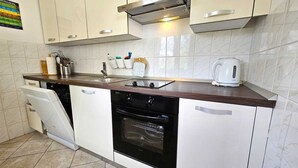 Une cuisine moderne avec des meubles blancs, un four noir, une hotte en acier inoxydable et une bouilloire blanche posée sur le plan de travail.