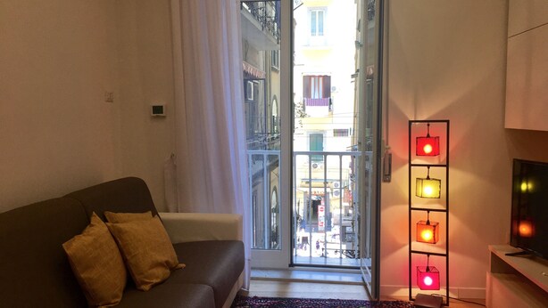 A living room with a sofa, a colorful rug, a TV stand, and a door leading to a balcony. - "G&G Pignasecca" house in the heart of central Naples (Napoli)