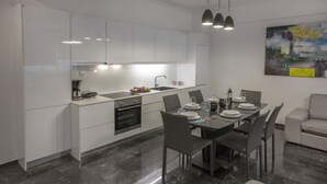 Une cuisine moderne avec des meubles blancs, un coin repas avec une table dressée pour quatre personnes, et un canapé gris.