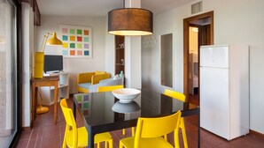 Een moderne keuken met een eettafel, gele stoelen, een witte koelkast en een kleurrijk kunstwerk aan de muur.