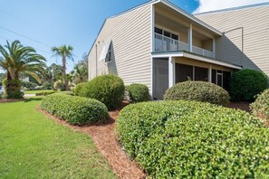 A two-story building with a balcony on the second floor, surrounded by well-maintained hedges and a lawn. - Bayou Village 613 (Miramar Beach)