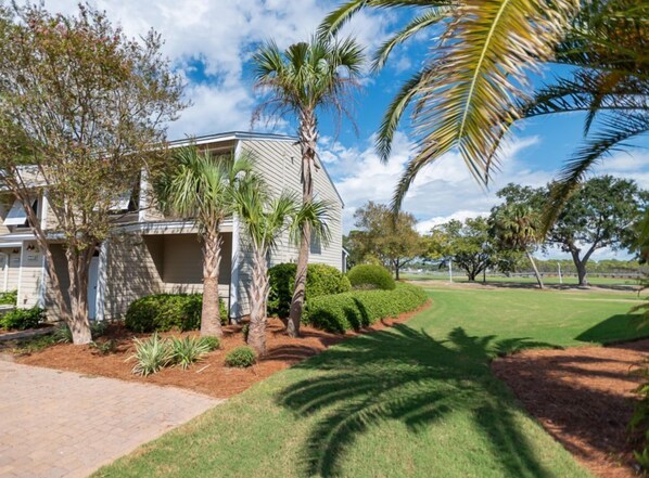 A two-story house with a sloped roof, surrounded by a well-maintained lawn and palm trees. - Bayou Village 613 (Miramar Beach)