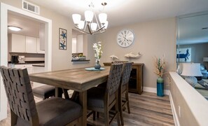 A dining area with a wooden table and chairs, a chandelier, a clock, and a vase with flowers. - Bayou Village 613 (Miramar Beach)