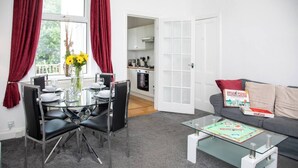 A modern living room with a glass dining table, black chairs, a grey sofa, and a Monopoly board game. - Glebe Street Apartment (Fife)