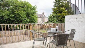 An outdoor patio with wicker chairs and a table, a wooden fence, and a white wall. - Glebe Street Apartment (Fife)