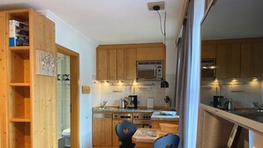 Cocina compacta con armarios de madera, un microondas y un comedor con dos sillas.