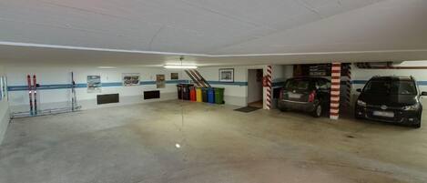 Een parkeergarage met twee geparkeerde auto's, een ski-drager en kleurrijke afvalbakken.