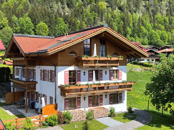 A two-story chalet with wooden balconies, a red-tiled roof, and a stone foundation.
