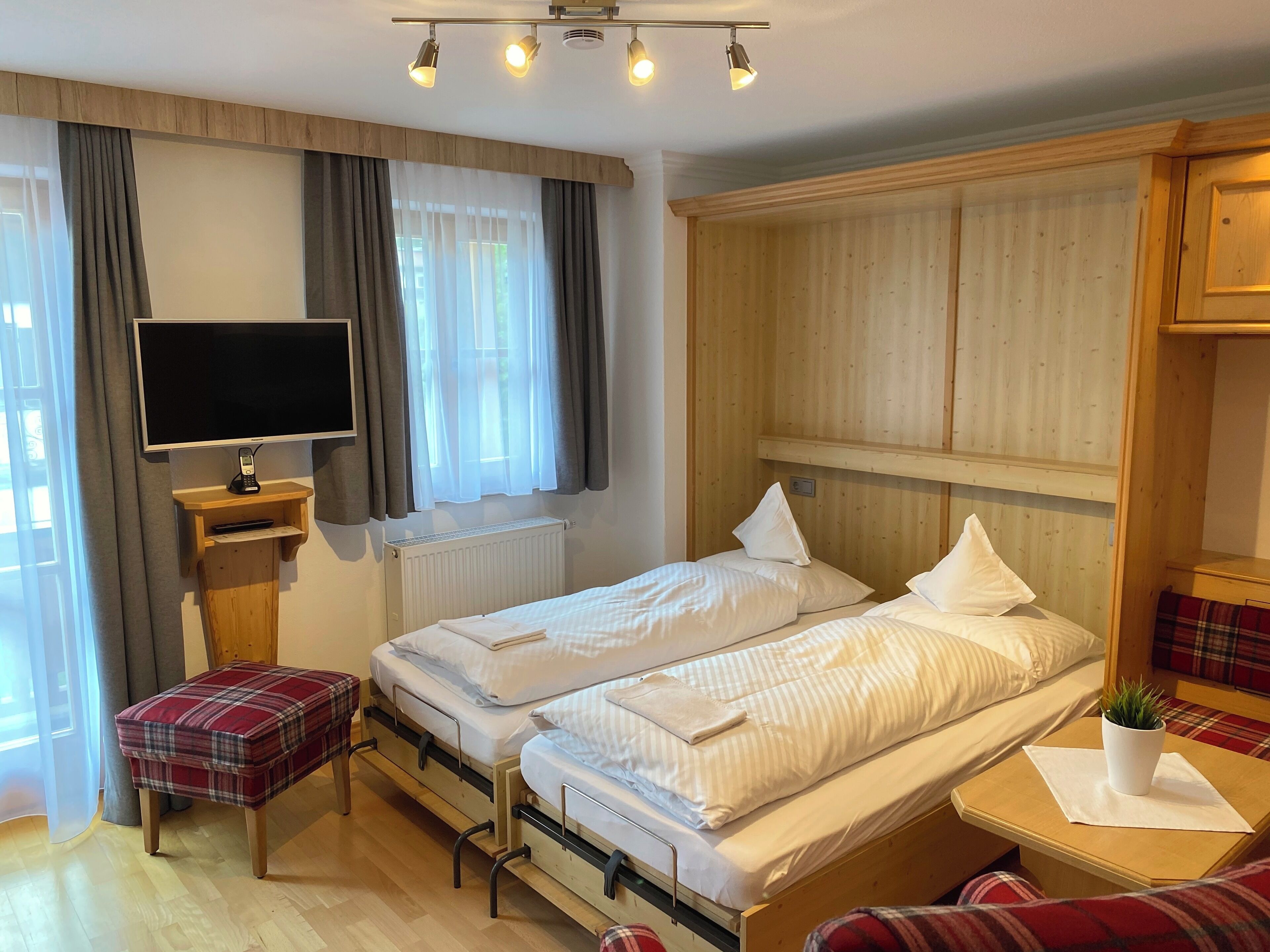 A hotel room with two beds, a TV, a small table with a plant, and a window with curtains.