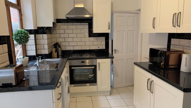 A modern kitchen with white cabinets, a black countertop, a stainless steel stove, and a built-in oven. - Gordon House. (Kettering)