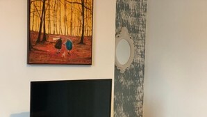 A television on a yellow stand, a painting of two figures in a forest, and a wall with a circular cutout. - Gordon House. (Kettering)