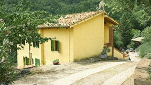 A yellow building with a tiled roof, a satellite dish, and a paved driveway.