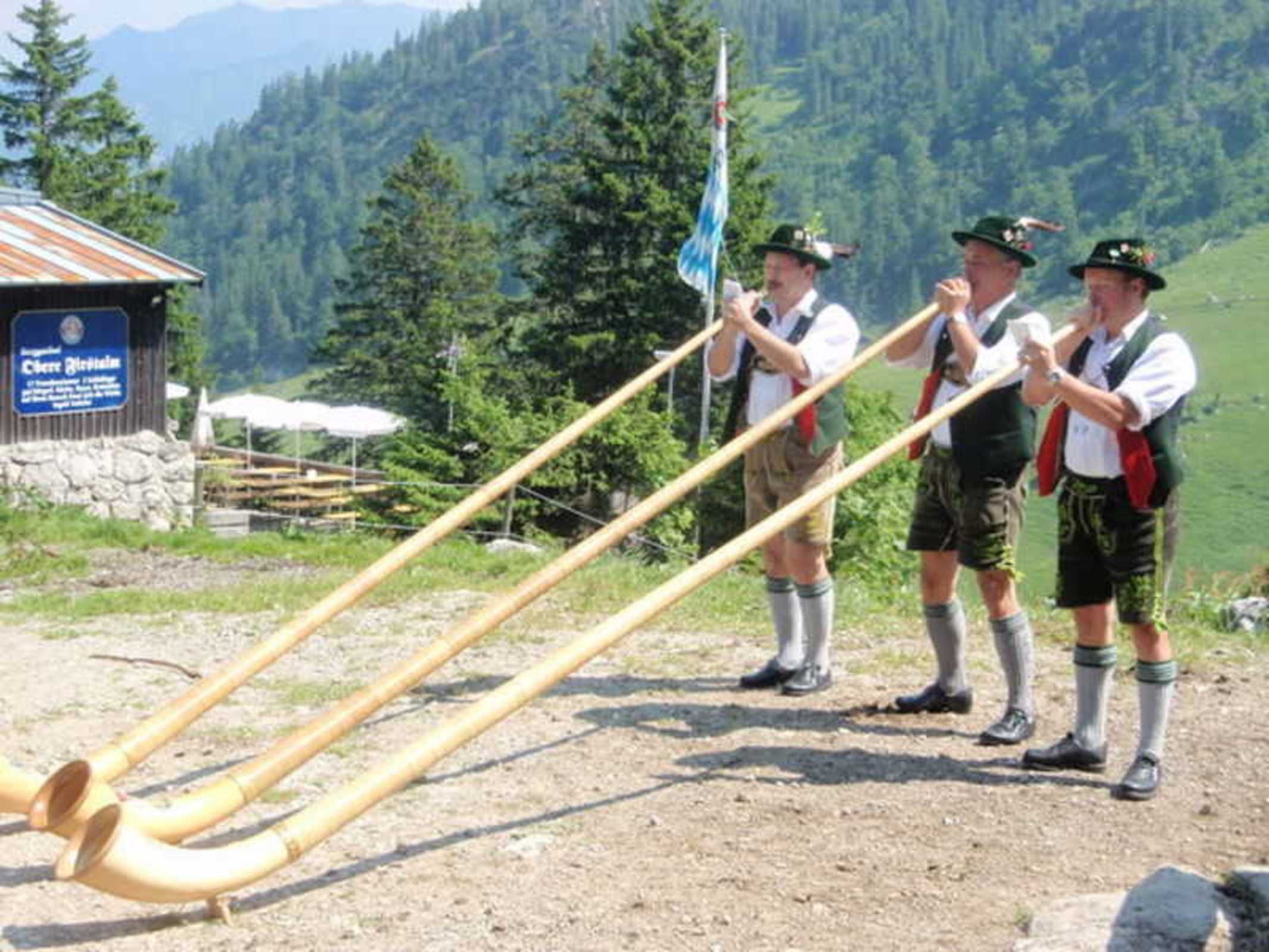 Three individuals in traditional attire standing next to a large wooden structure with pipes.