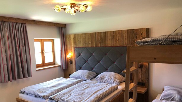 A wooden bunk bed room with a window, curtains, and a chandelier.