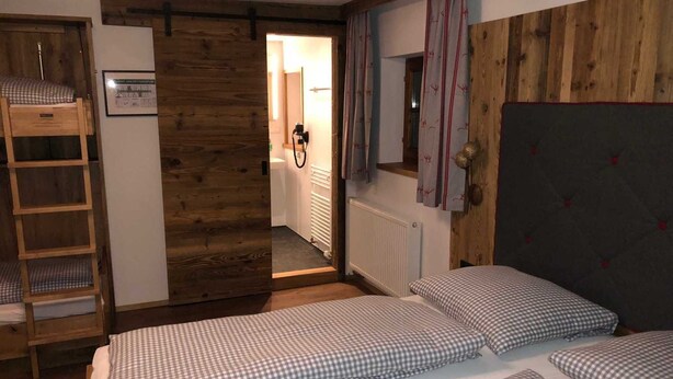 Ein Zimmer mit zwei Betten, einem Holzschrank, einem Heizkörper und einer Tür zu einem anderen Raum.