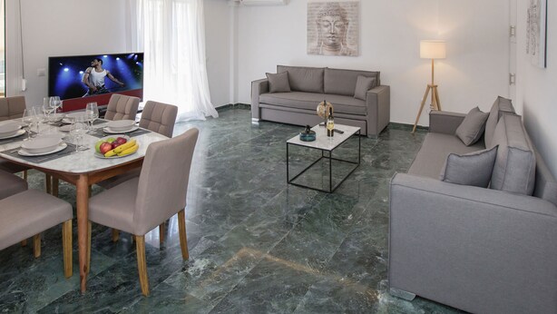 Una sala de estar moderna con televisor de pantalla plana, un sofá gris, una mesa de comedor con platos y vasos, y una mesa de centro.