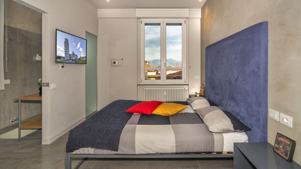 A modern bedroom with a bed, a TV, a window with a view, and a radiator. - Mediceo 42 - Deluxe Double Room (Pisa)