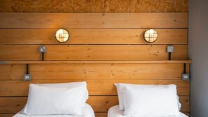 Une chambre avec deux lits, chacun doté de draps blancs et d’une tête de lit en bois. On y trouve deux appliques murales avec des abat-jour en verre rond.