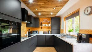 Une cuisine moderne avec des meubles de couleur noire, un plafond en bois et une fenêtre donnant sur un paysage verdoyant.