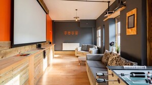 Un salon moderne avec un canapé, une table basse et un baby-foot. Il y a une cheminée et une fenêtre donnant sur un beau paysage.