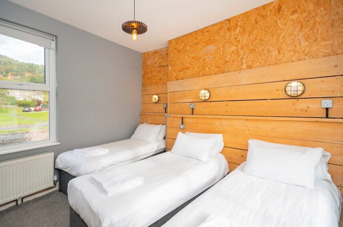 A hotel room with two single beds, a wooden headboard, a large window with a view of a green landscape, and a modern light fixture.