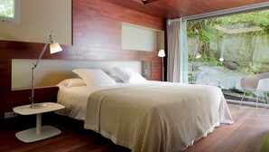 A modern bedroom with a large bed, bedside lamps, and a view of a garden through a glass door. - Villa Baena by FeelFree Rentals (San Sebastián)