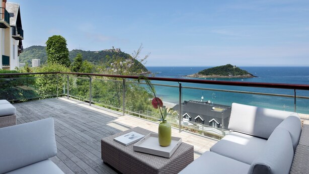 A balcony with outdoor seating, a vase, and a view of the sea and a distant island. - Villa Baena by FeelFree Rentals (San Sebastián)