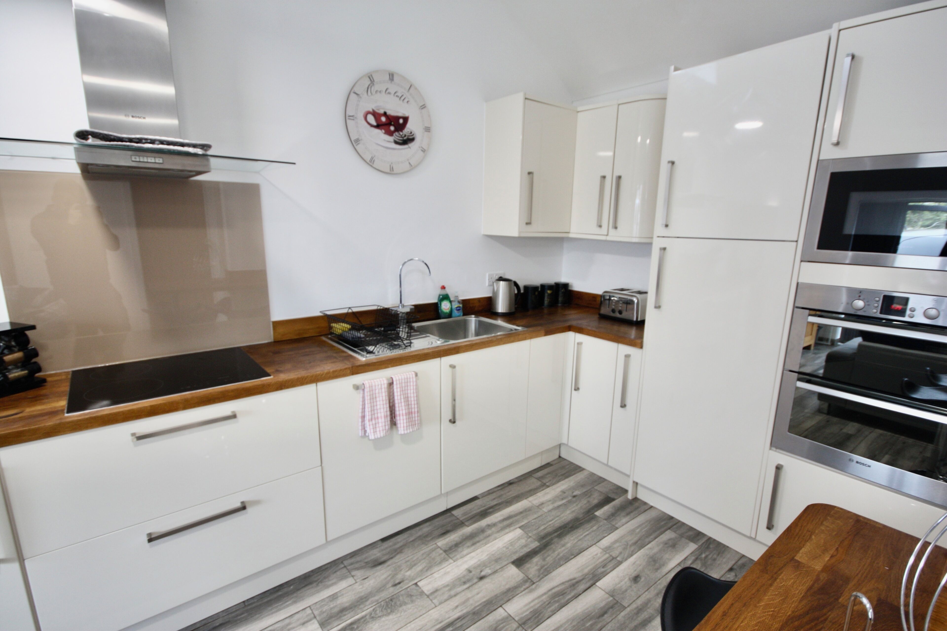 Una cocina moderna con armarios blancos, campana extractora de acero inoxidable, horno empotrado y encimera de madera.