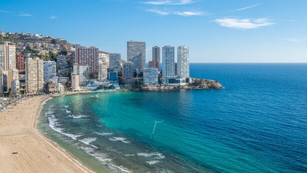 Un paisaje urbano costero con edificios altos, una playa de arena y aguas azules cristalinas.