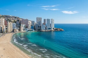 Un paisaje urbano costero con edificios altos, una playa de arena y aguas azules cristalinas.