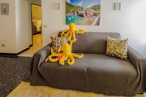 A living room with a sofa, a large octopus plush toy, and two framed pictures on the wall.
