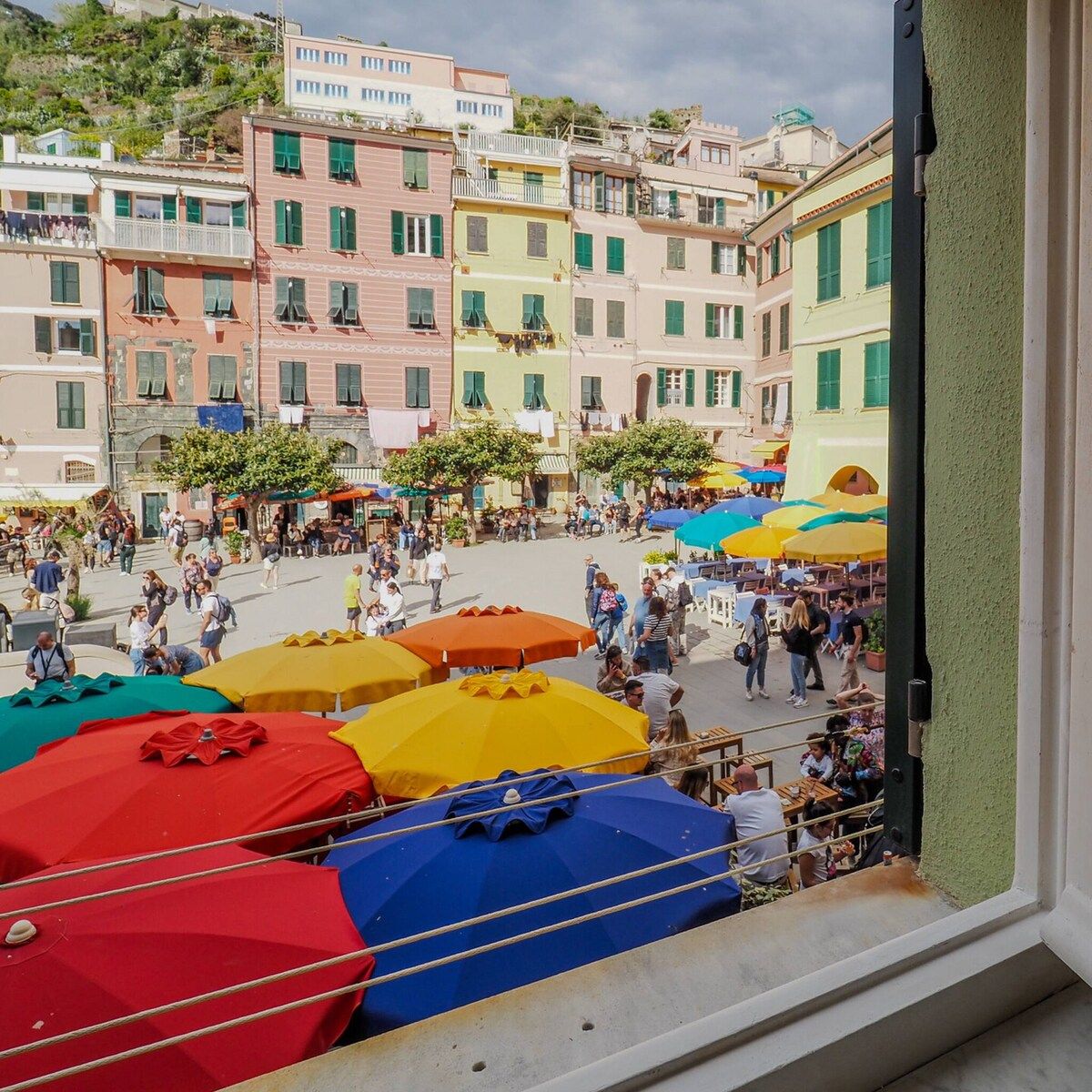 Une place animée, avec des parasols colorés, des gens qui se promènent et des bâtiments dotés de balcons.