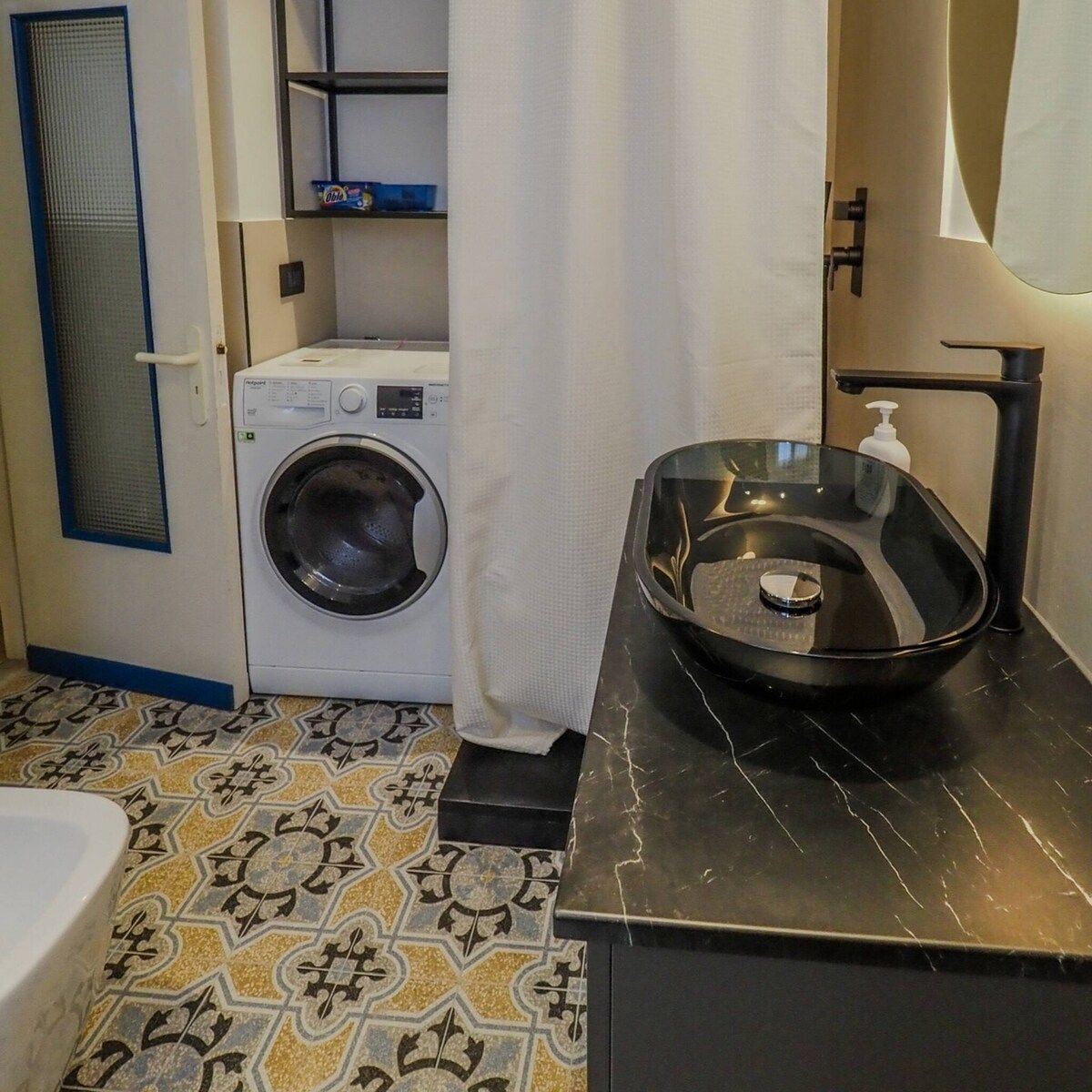 A bathroom with a washing machine, a black sink with a marble-like basin, and patterned floor tiles.