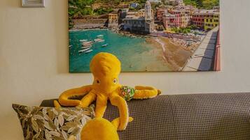 Una habitación con un sofá, un cuadro enmarcado de un pueblo costero y un peluche de pulpo.