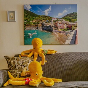 Una habitación con un sofá, un cuadro enmarcado de un pueblo costero y un peluche de pulpo.