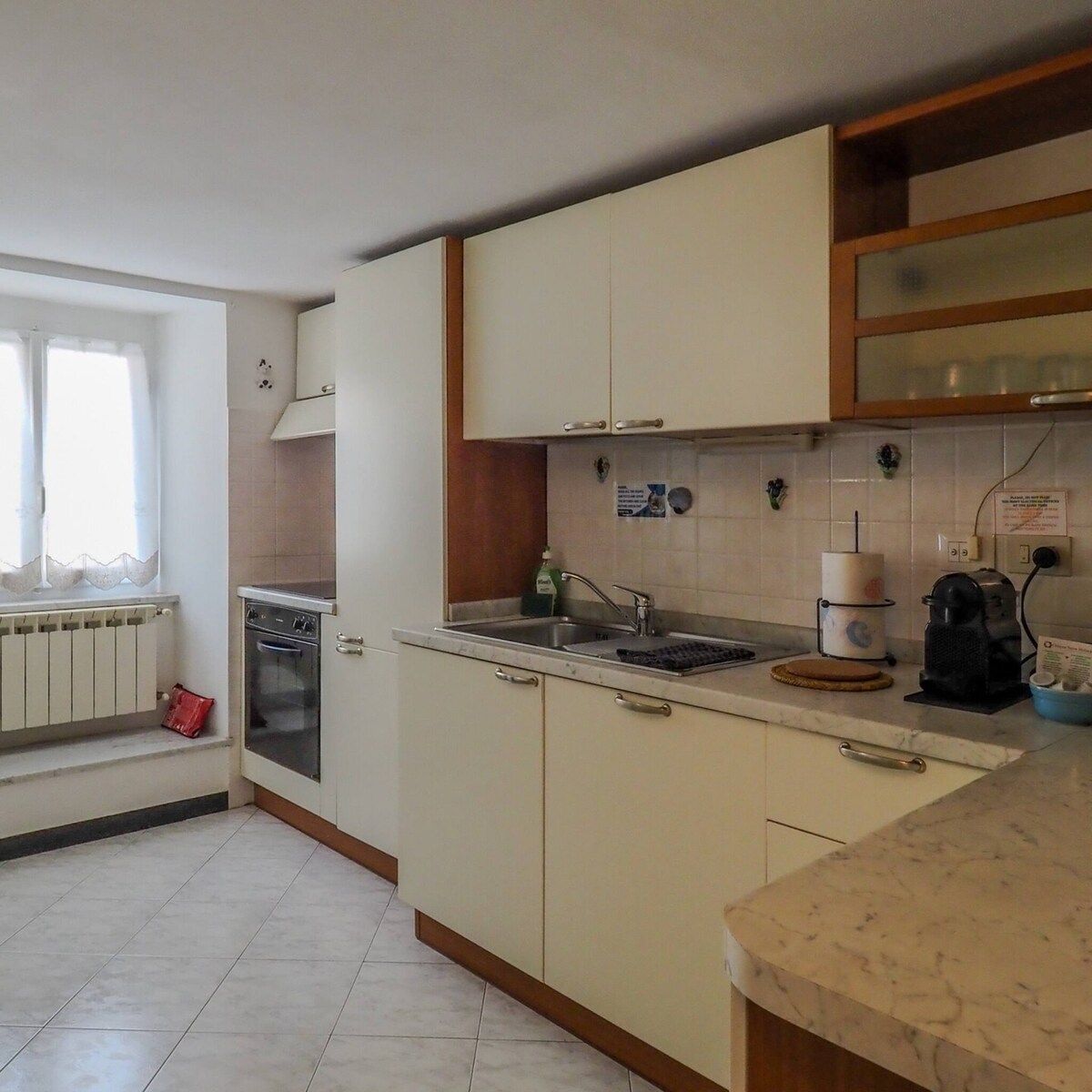 Une cuisine avec des meubles blancs, un évier, une cuisinière et une fenêtre avec des rideaux.