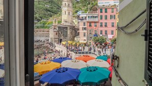 Une vue d’une ville côtière avec des bâtiments aux couleurs vives, un beffroi et une plage animée, parsemée de parasols.