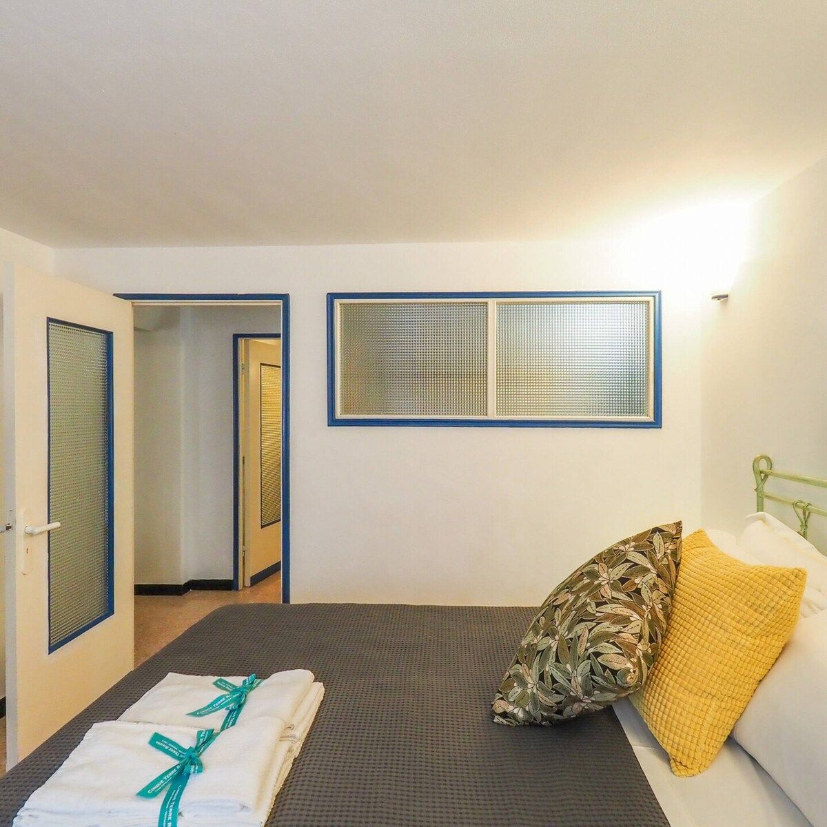 Une chambre d’hôtel avec un lit, une fenêtre avec des stores, une porte et une salle de bain visible à travers une porte ouverte.