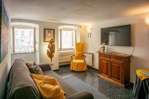 A cozy living room with a sofa, a yellow armchair, a wooden cabinet, and a TV mounted on the wall.