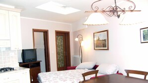 A compact room with a bed, a dining table, a TV, and a kitchenette.