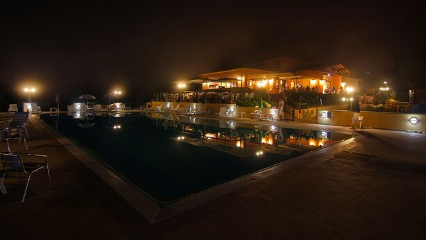 A nighttime pool area with lounge chairs and a building with lights.